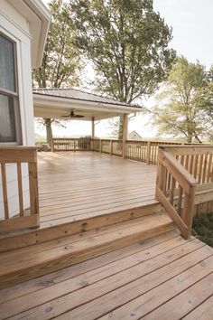 a wooden deck with steps leading up to the front door and covered porch area next to trees