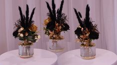 three vases filled with flowers and feathers on top of a white tablecloth covered table