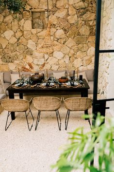 a dining table with chairs and plates on it in front of a stone wall,