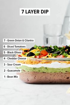 the ingredients for a layered layer dip in a glass dish on a counter top with chips and guacamole