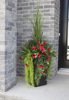 a black planter with red flowers and greenery in front of a brick wall