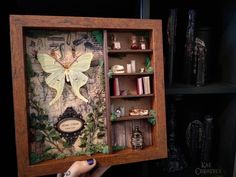 a person holding up a wooden box with an image of a butterfly on the inside