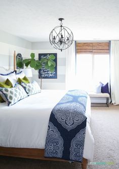 a white bed with blue and green pillows on top of it next to a window