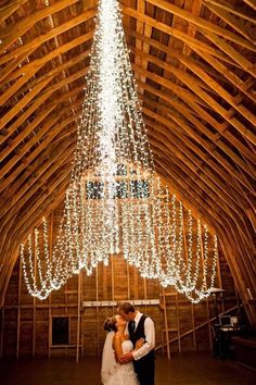 a bride and groom standing in front of a chandelier at their barn wedding