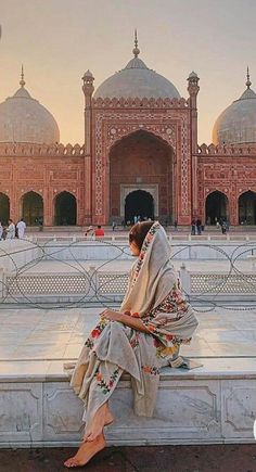 a woman sitting on a bench in front of a building with many arches and domes