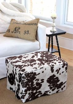 a cow print ottoman sits in front of a white couch with a pillow on it