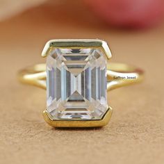 an emerald cut diamond sits on top of a gold ring