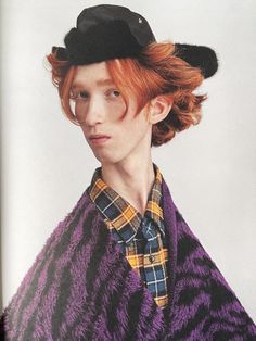 a young man with red hair wearing a black hat and plaid shirt, standing in front of a white background