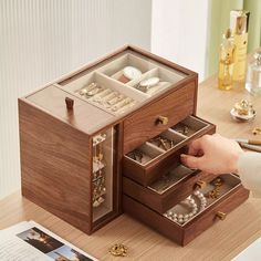 a wooden jewelry box is open on a table next to a woman's hand