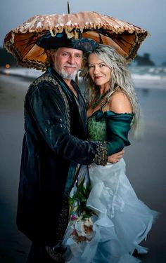 a man and woman are standing on the beach under an umbrella