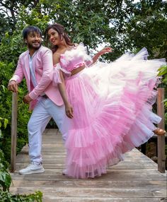 a man and woman dressed in pink posing for the camera on a wooden bridge surrounded by greenery