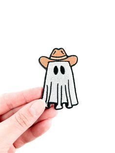 a hand holding a small patch with a ghost wearing a hat