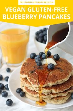 a stack of pancakes with syrup being poured on top and blueberries in the background