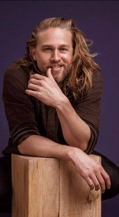 a man sitting on top of a wooden block with his hand under his chin and looking at the camera