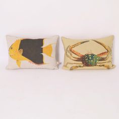 two pillows with crabs and fish on them sitting next to each other in front of a white wall