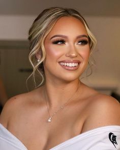 a woman with blonde hair wearing a white top and diamond necklace smiling at the camera