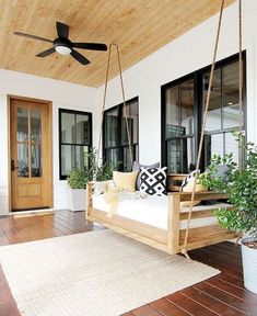 a porch with a swing bed and potted plants on the front porch, along with a ceiling fan