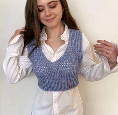 a woman wearing a blue knitted vest and holding her hands behind her back to the camera