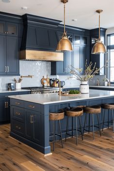 a large kitchen with blue cabinets and gold pendant lights hanging from the ceiling, along with bar stools