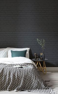 a bed with white sheets and pillows in front of a black brick wall next to a night stand