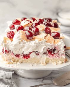 a cake with cherries and whipped cream on top sitting on a plate next to a fork