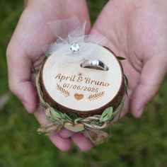 two hands holding a wooden ring box with wedding rings on it and an arrow in the middle