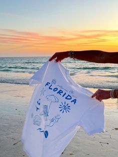 Our EXCLUSIVE Greetings From Florida Sunhoney T-shirt is perfect for beach lovers! This Comfort Colors t-shirt features a playful blue drawn design of popular Florida symbols like the sun, shell, mermaid, and more. Style this shirt over your fave bikini as your new go-to beach tee or style with biker shorts and sneakers for the cutest summer fit! Designed by us, handmade by us in Jacksonville Beach, FL Product is made to order: available for pick up/ships in 2-4 business days Content: 100% Cotto Blue Beachwear T-shirt For Beach Party, Blue T-shirt For Beach Party, Beachwear Style, Vacation Cotton T-shirt With Custom Print, Fun Custom Print Tops For Beach Season, Custom Print White T-shirt For Summer, Blue Short Sleeve T-shirt For Beach Party, Cotton Beachwear T-shirt For Summer Adventures, Cotton Beachwear T-shirt For Summer, Beach Season Graphic Tee With Custom Print