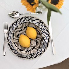 two lemons in a bowl on a table with silverware and sunflowers