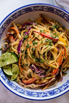 a blue and white bowl filled with noodles, carrots, onions and cilantro