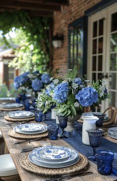 a table set with blue and white plates and vases filled with hydrangeas