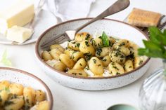 two bowls filled with pasta and cheese on top of a white table next to silverware