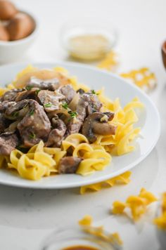 a white plate topped with pasta covered in mushrooms and sauce next to bowls of eggs