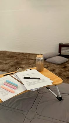 a wooden table with papers and pens on it next to a jar of liquid, notebooks and pen