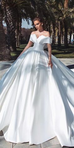 a woman in a white wedding dress is walking down the street with palm trees behind her