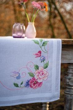 two vases with flowers are sitting on a table next to a cross - stitch tablecloth