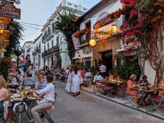 people are sitting at tables in an outdoor cafe area with flowers growing on the buildings