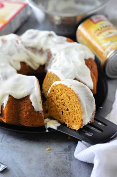 a bundt cake with white frosting on a black plate next to cans of orange juice