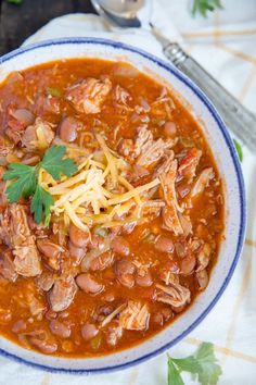 a white bowl filled with chili and chicken soup on top of a table next to a spoon