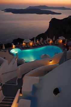 an outdoor swimming pool next to the ocean at dusk with umbrellas and chairs around it