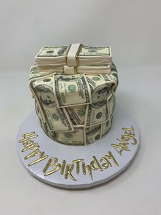 a birthday cake made out of money on top of a white plate with the words happy birthday written in gold lettering