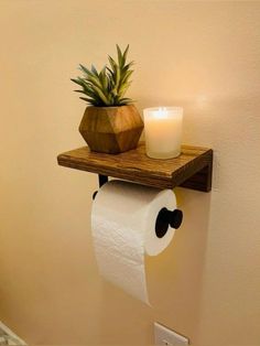 a toilet paper holder with a candle on it and a potted pineapple in the corner