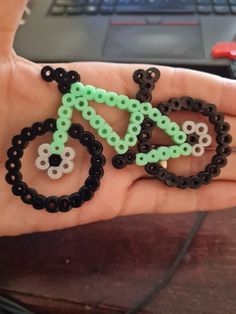 a hand holding a small beaded bicycle on it's palm with a laptop in the background