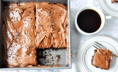 a cake with chocolate frosting in a pan on a table next to two cups of coffee