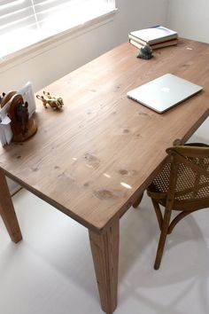 a wooden table with a laptop on top of it next to a chair and window