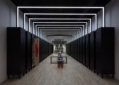 a man sitting on a bench in the middle of a hallway with black lockers