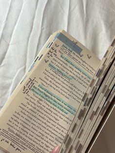 an open book sitting on top of a bed next to a hand holding a pen