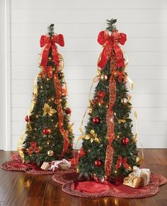 two christmas trees decorated with red and gold ribbons, bows and ornaments are on the floor next to each other