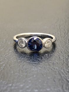 DeKara Designs Collection Beautiful Modern/Art Deco Ceylon Blue Sapphire and Diamond Ring Metal- 90% Platinum, 10% Iridium Stones- 1 Round Ceylon Blue Sapphire 1.00-1.05 Carats 6 MM, 2 Round Diamonds F-G VS2 Clarity, 0.40 Carats. Size-4-12 Classic and Timeless Art Deco Inspired Ceylon Blue Sapphire Diamond Three Stone Engagement Ring. There is a beautiful Ceylon Blue Sapphire that is extremely fiery and amazing in color that is featured as the center stone. The blue sapphire is professionally be Blue Sapphire Three-stone Promise Ring, Blue Three Stone Sapphire Promise Ring, Blue Diamond Platinum Ring With Polished Finish, Blue Platinum Diamond Ring With Polished Finish, Luxury Rings With Polished Lab-created Sapphire, Blue Topaz Ring With Accent Stones In Platinum, Platinum Blue Three Stone Rings, Luxury Three Stone Sapphire Ring, Elegant Blue Three Stone Sapphire Ring