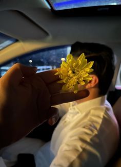 a man holding a flower in his hand while sitting in the back seat of a car