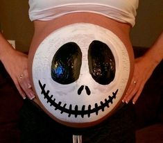 a pregnant belly with fake eyes and mouth painted to look like jack skellingy